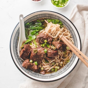Taiwanese beef noodle in a bowl with spoon and chopsticks.