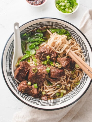 Taiwanese beef noodle in a bowl with spoon and chopsticks.