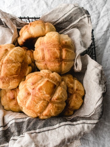 pineapple buns in a basket lined with dish towel over a white clothe.