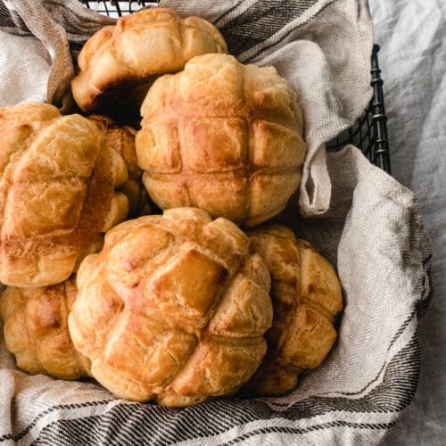 pineapple buns in a basket lined with dish towel over a white clothe.