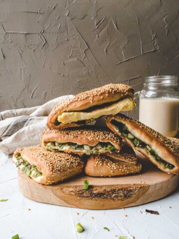 five scallion shaobing on a wood board and a cup of soy milk at the back.