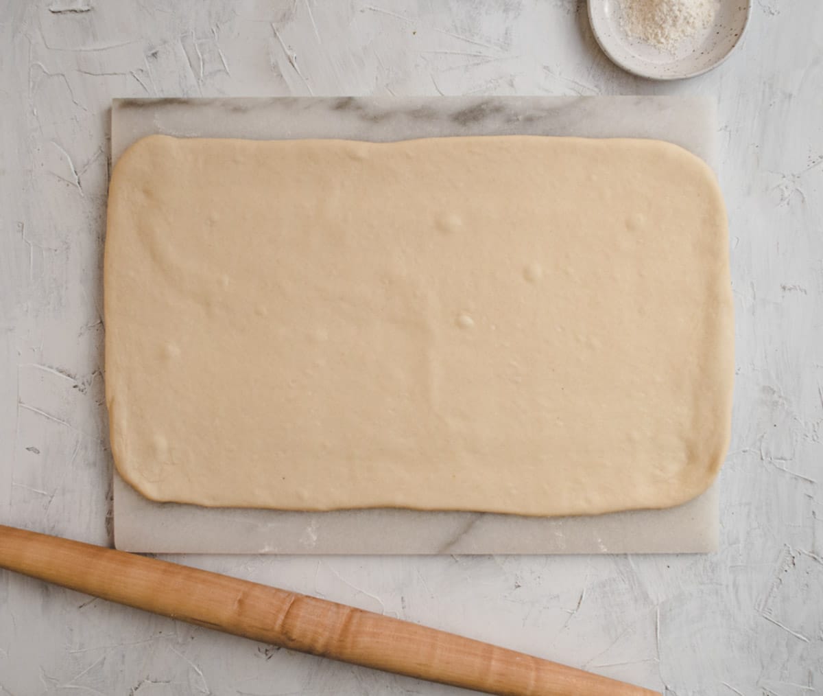 rolled out shaobing dough on a marble board with a small plate of flour and rolling pin.