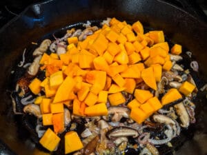 butternut squash cubes, mushroom and shallot in a black skillet.