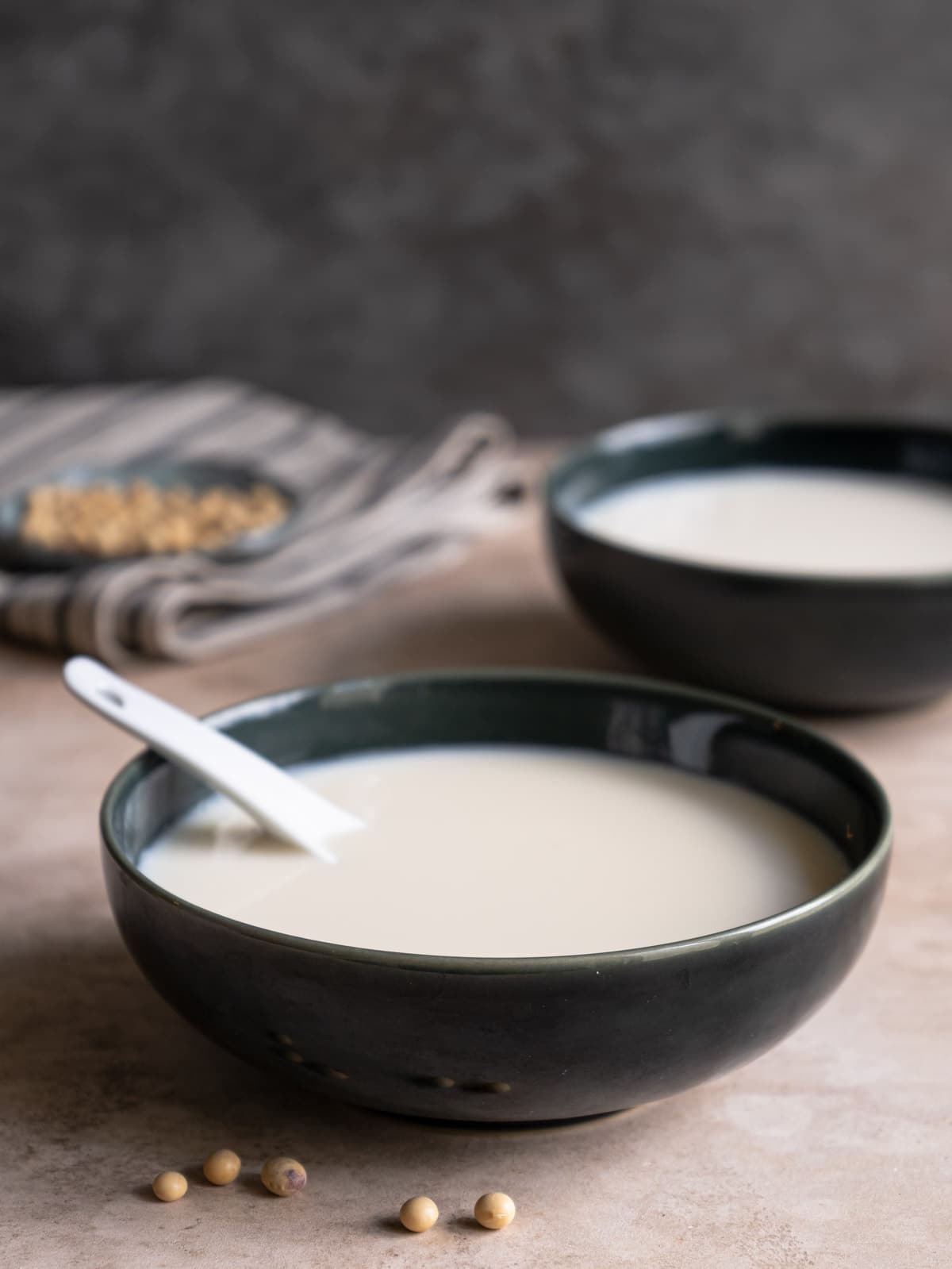 Two bowls of soy milk with a small plate of soy bean at the back.