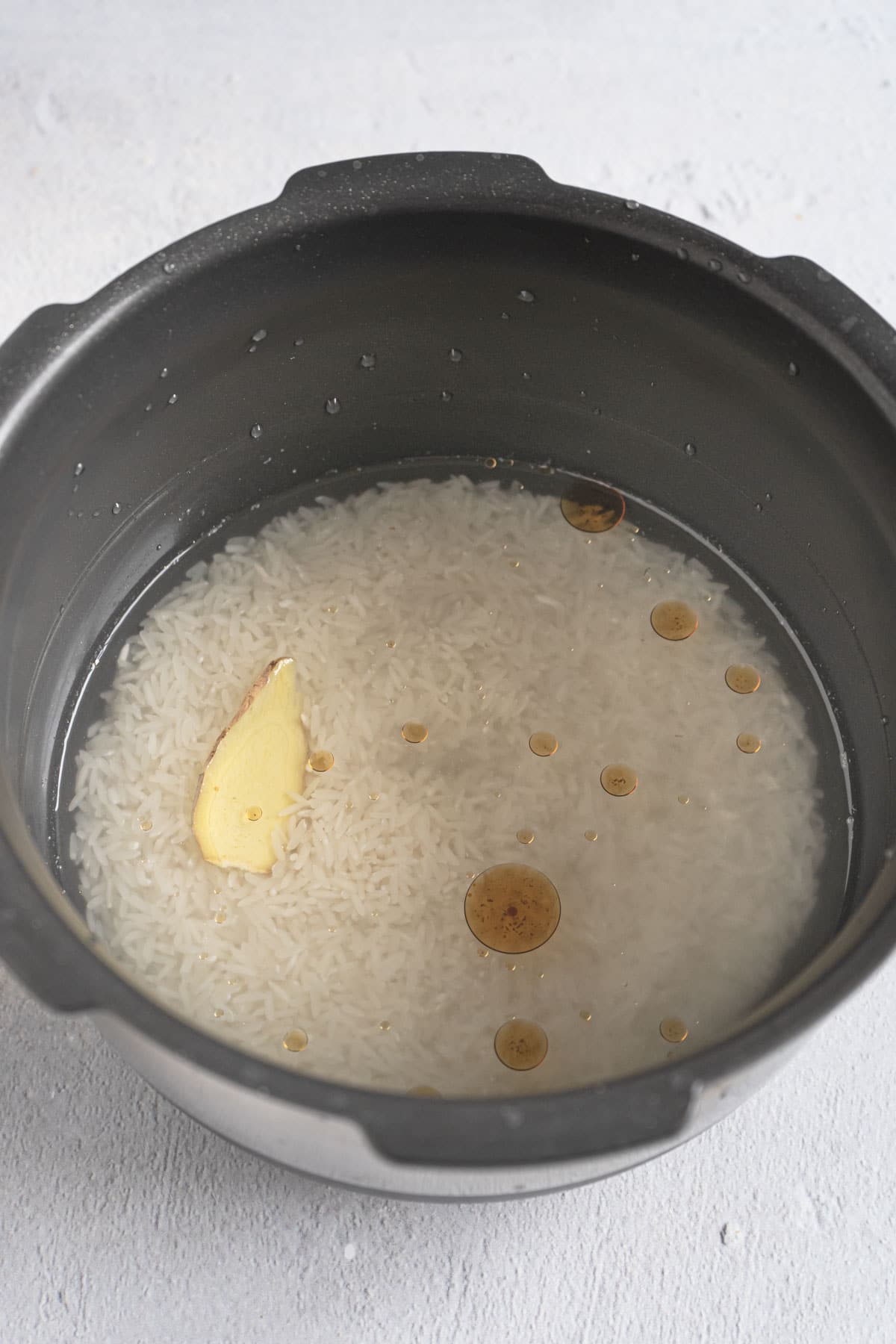 Rice cooker pot with white rice, ginger, sesame oil and water in it. 
