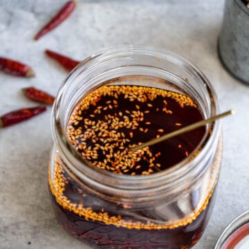 Homemade chili oil in a glass jar with chili pepper on the side.
