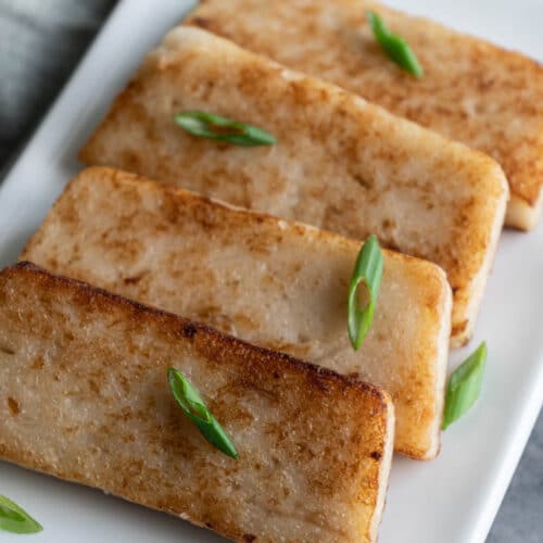 Four slices of turnip cake on a white plate sprinkled with chipped scallion.