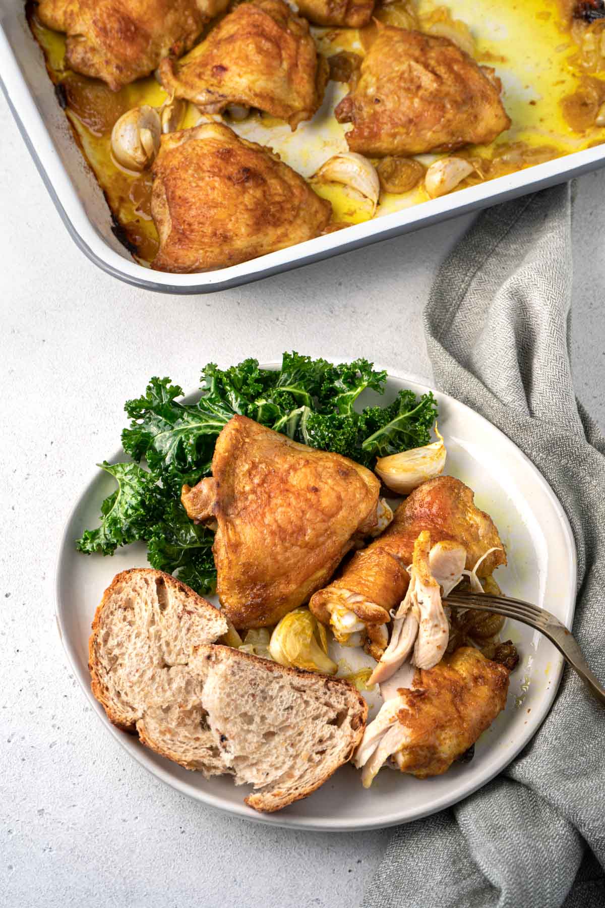 Baked chicken thighs, bread and kale salad on a plate. 