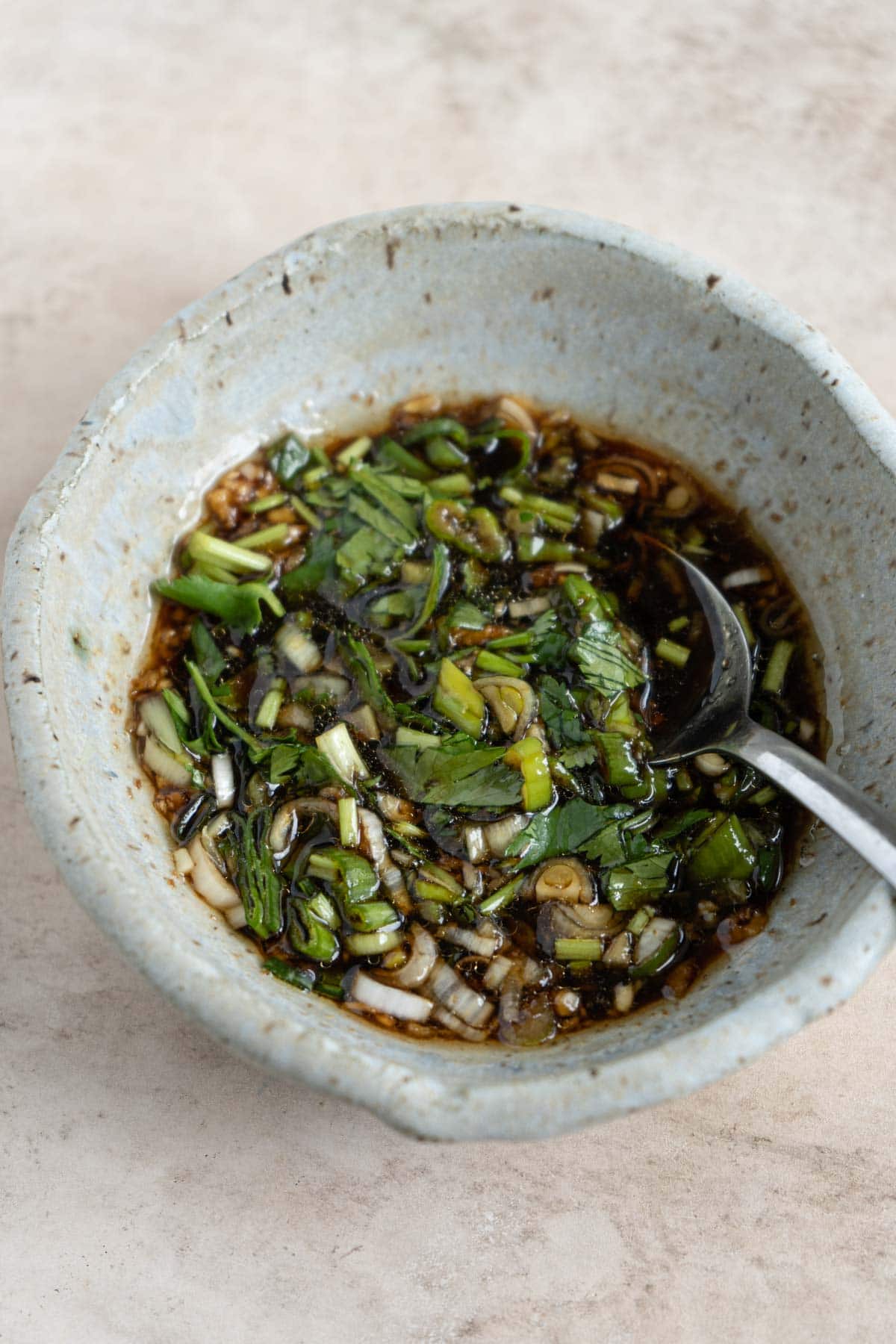 A bowl of garlic soy dressing with chopped scallion and cilantro. 