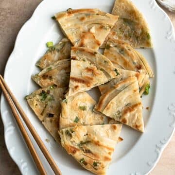 Scallion pancake slices in a white oval plate with a pair of chopsticks.