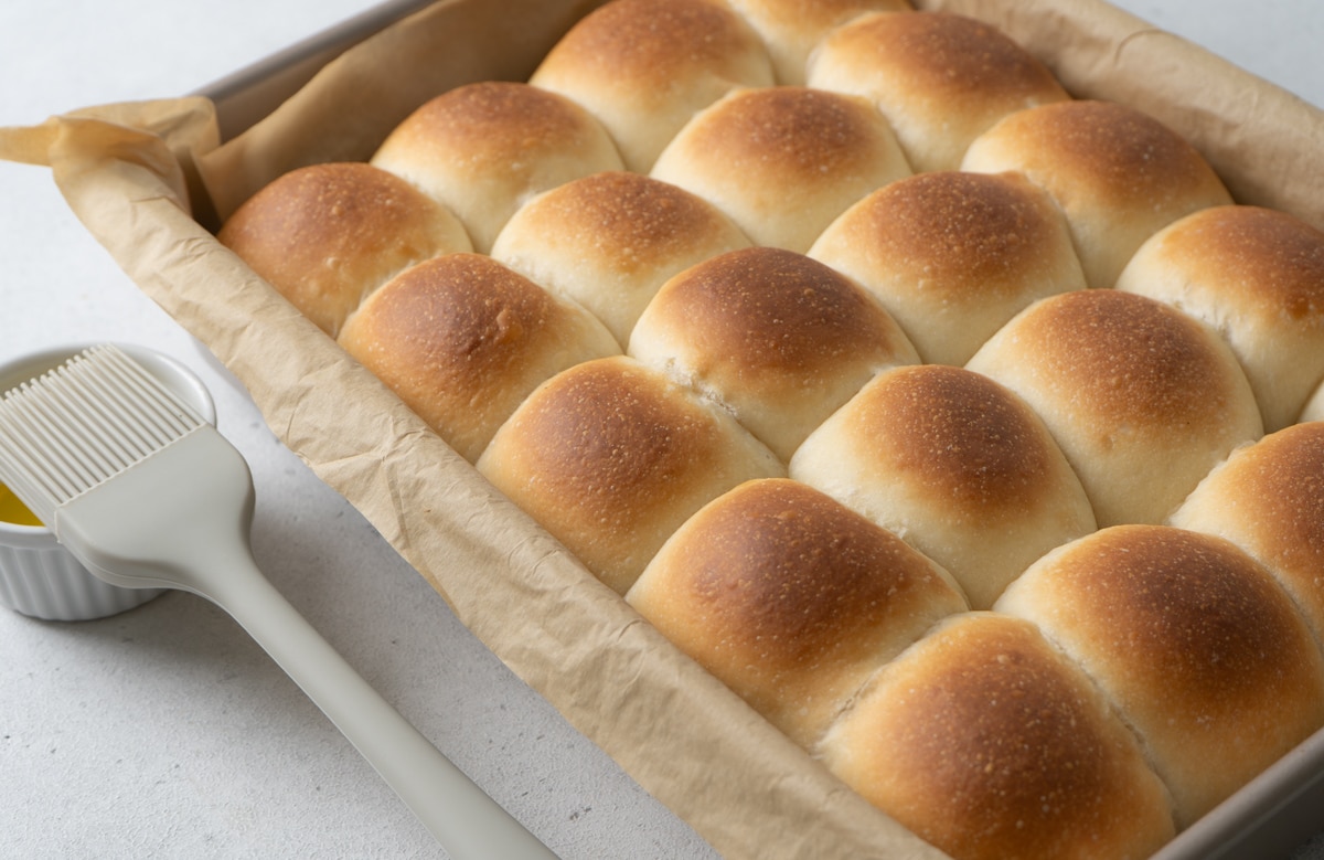Freshly baked dinner rolls in a tray with melted butter and pastry brush on the side. 