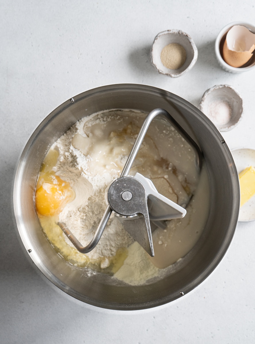 Bread dough ingredients in a stand mixer bowl with a dough hook.