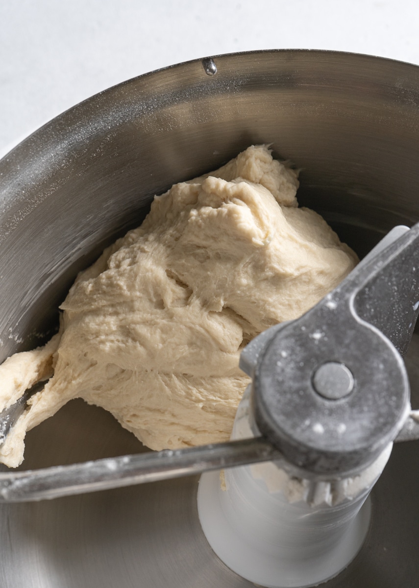 Bread dough in a stand mixer bowl with a dough hook.