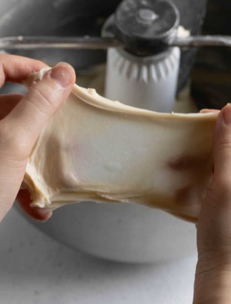 Hands stretching bread dough to check the windowpane test.