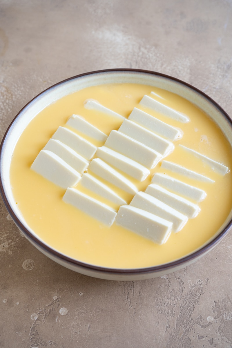 Sliced tofu neatly arranged in a bowl filled with a smooth, uncooked egg mixture.