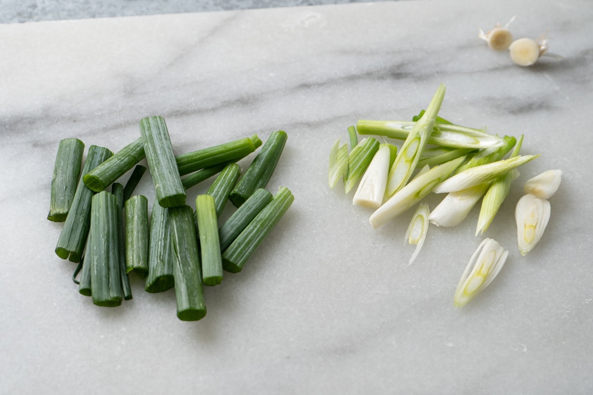 Chopped green onions on a marble surface. Dark green parts cut into 2-inch pieces and white parts sliced diagonally.