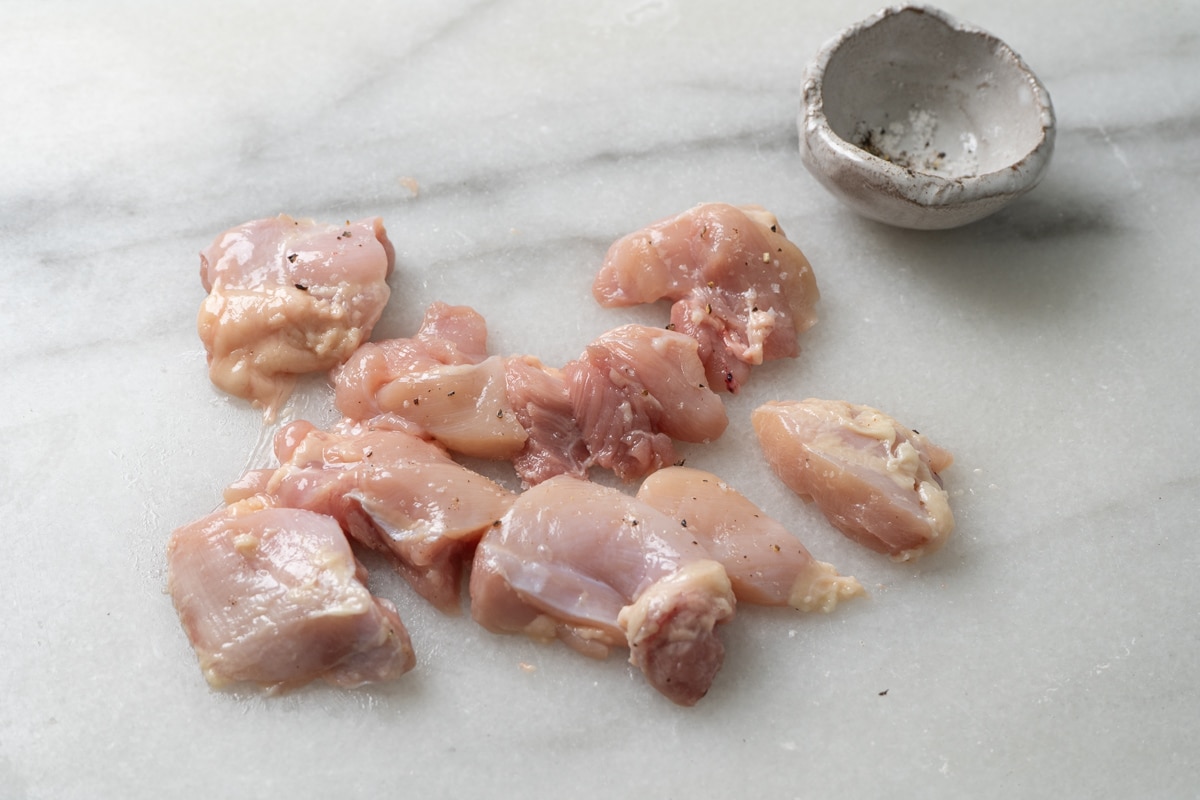 Small chicken pieces sprinkled with salt and pepper, and a small bowl on the side.