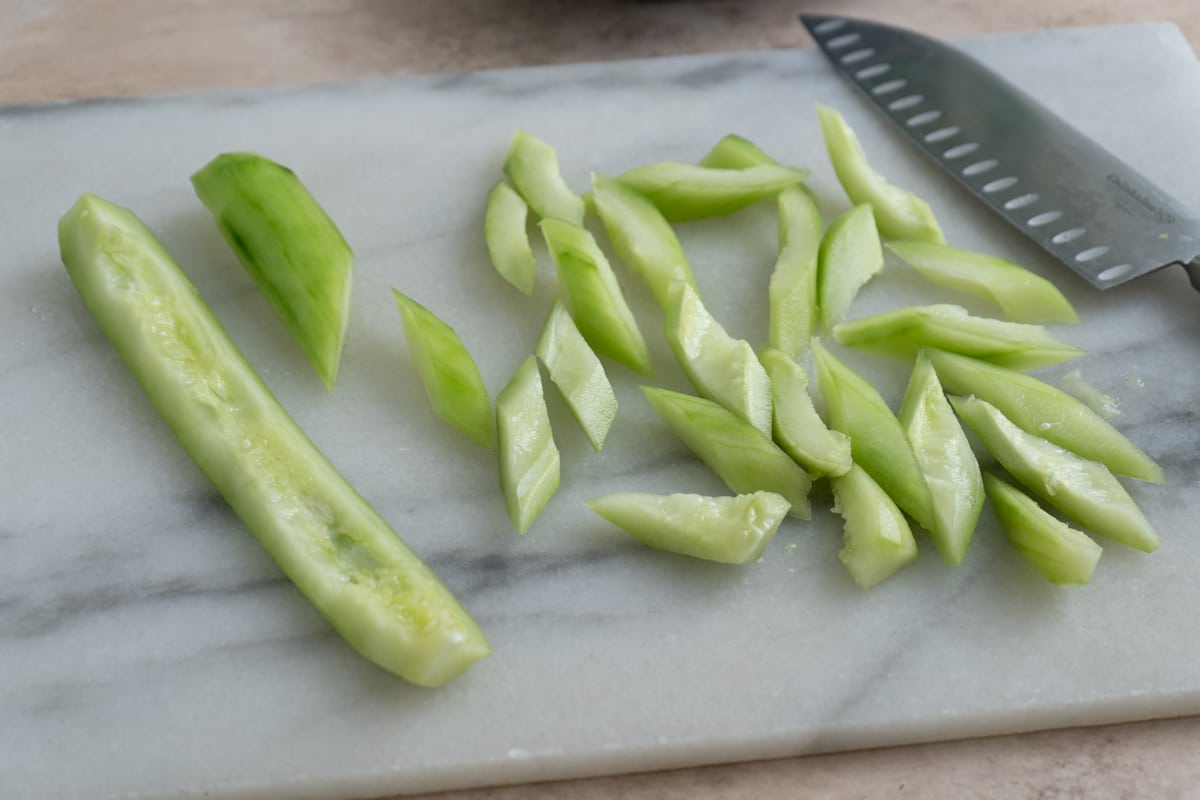 Seeded cucumber halves cut into angled slices on a marble cutting board, with a knife nearby.