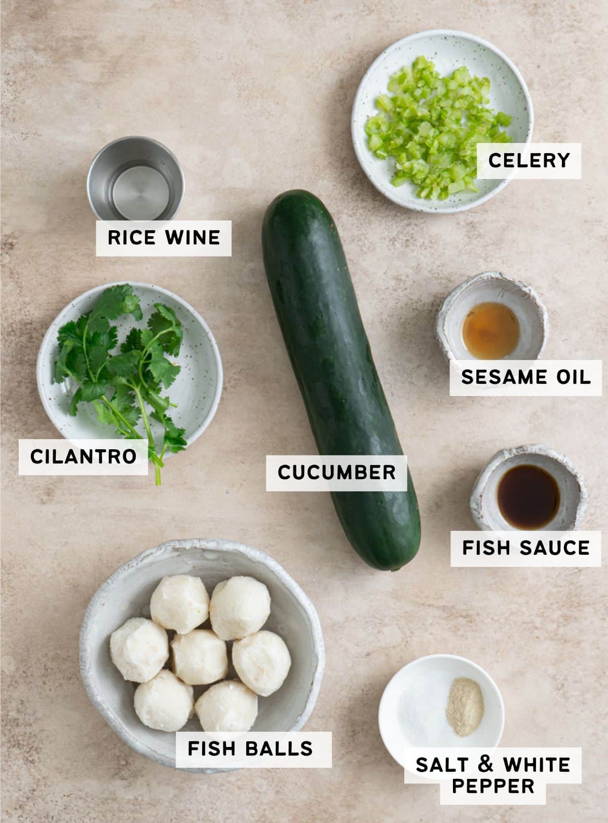 A cucumber in the middle with a bowl of 7 fish balls, a small plate of cilantro, a small plate of minced cilantro, and some seasoning ingredients on the side.