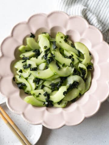 Cucumber and seaweed salad in a pink flower shape plate with a pair of chopsticks on the side.