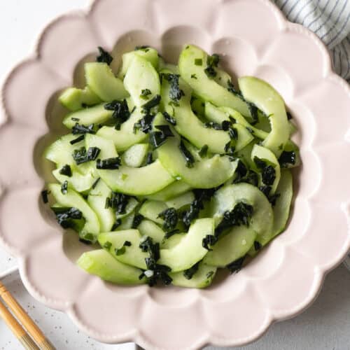 Cucumber and seaweed salad in a pink flower shape plate with a pair of chopsticks on the side.