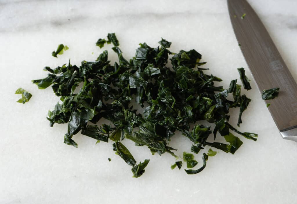 Rehydrated seaweed chopped into small pieces on a marble cutting board next to a knife.