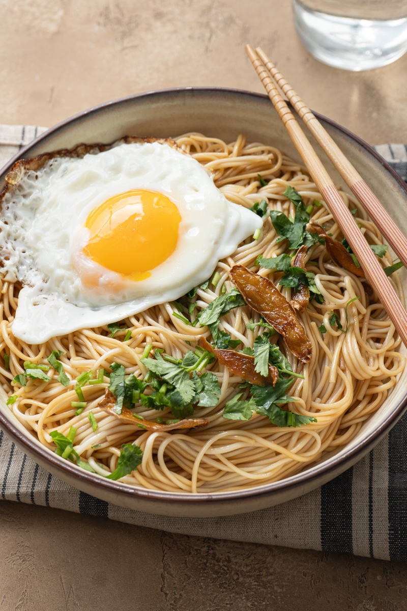 A bowl of ginger soy noodles top with fried egg, ginger pieces and cilantro.
