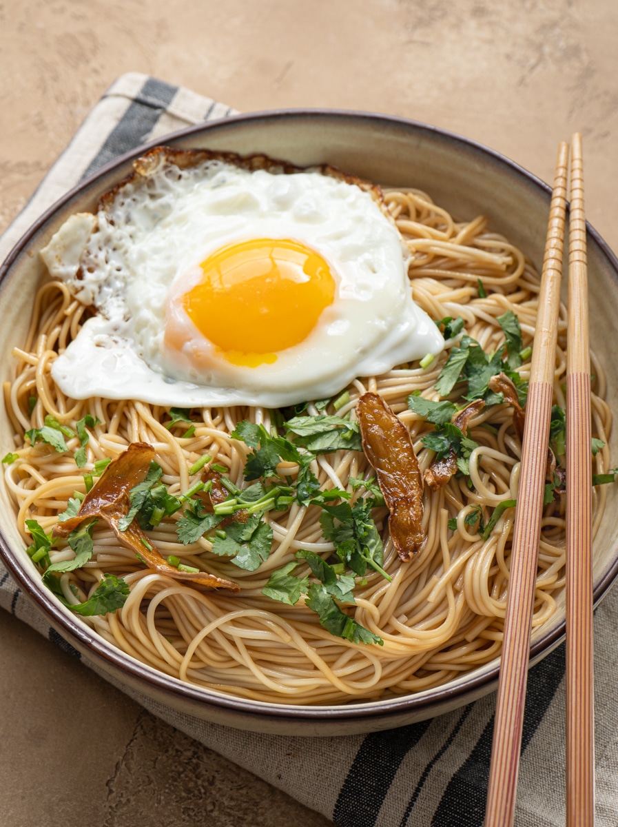 Ginger soy noodles topped with a fried egg and cilantro in a bowl.