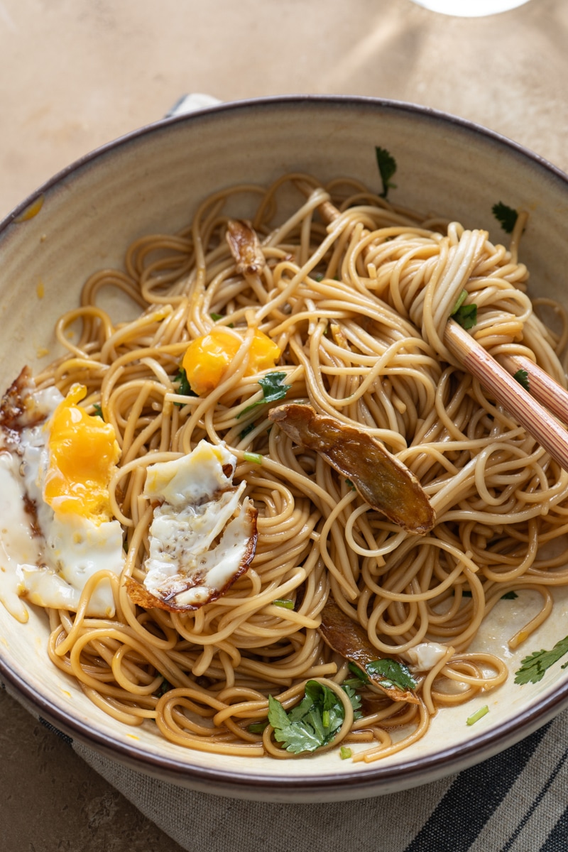 A bowl of ginger soy noodle, with fried egg pieces, ginger slices and cilantro.